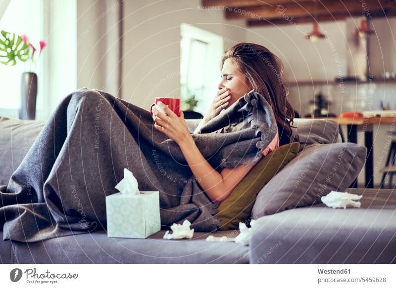 Porträt einer Frau, die krank auf dem Sofa liegt, hustet und versucht, heißen Tee zu trinken Tees sitzen sitzend sitzt junge Frau junge Frauen Erkältung