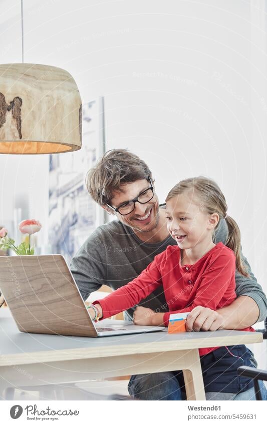 Glückliche Vater und Tochter mit einer Karte mit Laptop auf dem Tisch zu Hause Gemeinsam Zusammen Miteinander glücklich glücklich sein glücklichsein Zuhause