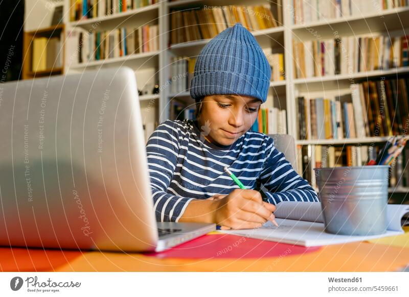Lächelnder Junge mit Strickmütze schreibt in Buch, während er zu Hause sitzt Farbaufnahme Farbe Farbfoto Farbphoto 10-11 Jahre 10 bis 11 Jahre 10 - 11 Jahre