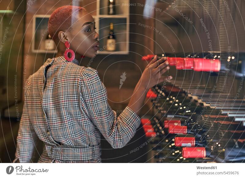 Junge Frau mit kurzem Haarschnitt wählt einen Wein in ihrem Keller Leute Menschen People Person Personen Afrikanisch Afrikanische Abstammung dunkelhäutig