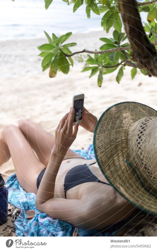Junge liegende Frau am Strand, die ein Smartphone benutzt lesen Lektüre junge Frau junge Frauen Beach Straende Strände Beaches iPhone Smartphones Meer Meere