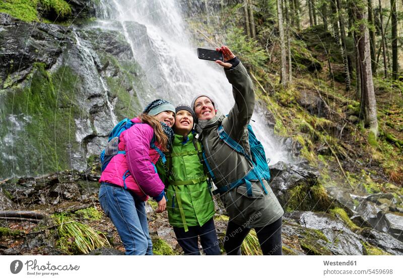 Lächelnde Frau nimmt sich mit Kindern gegen den Zweribach-Wasserfall im Nordschwarzwald Farbaufnahme Farbe Farbfoto Farbphoto Deutschland Außenaufnahme außen