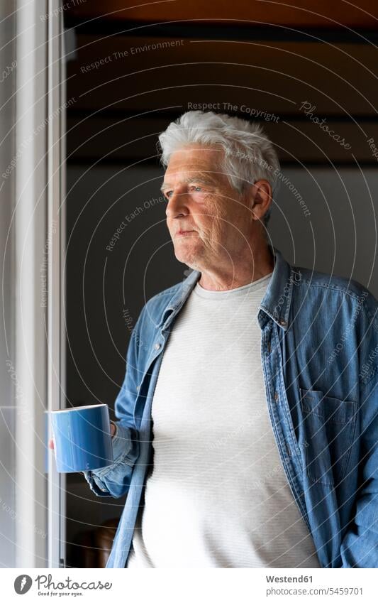 Nachdenklicher älterer Mann hält Kaffeetasse, während er zu Hause durchs Fenster schaut Farbaufnahme Farbe Farbfoto Farbphoto Innenaufnahme Innenaufnahmen innen