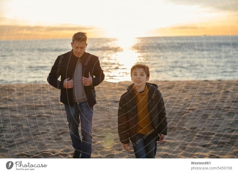 Vater und Sohn gehen bei Sonnenuntergang am Strand spazieren Beach Straende Strände Beaches Sonnenuntergänge Papas Väter Vati Vatis Papis gehend geht Söhne