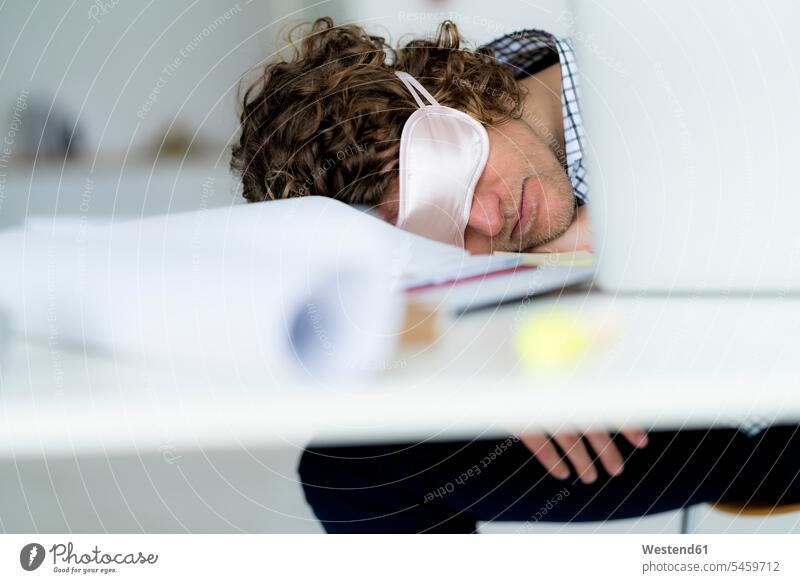 Überarbeiteter Geschäftsmann schläft am Schreibtisch und trägt eine Schlafmaske Businessmann Businessmänner Geschäftsmänner schlafen schlafend Büro Office Büros
