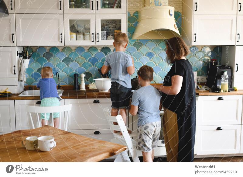 Mutter beim Kochen mit ihren drei Söhnen in der Küche Schale Schalen Schälchen Schüsseln T-Shirts Stuehle Stühle stehend steht daheim zu Hause Miteinander