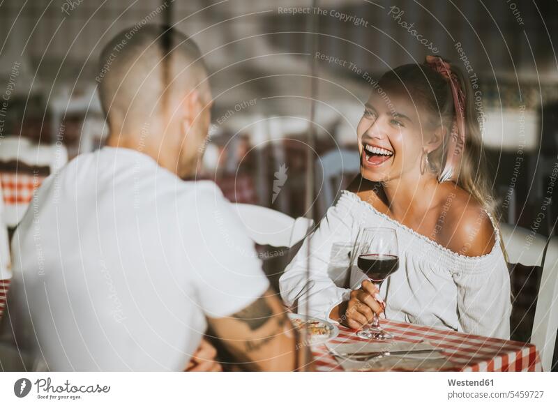 Glückliche Frau mit Weinglas in der Hand, die ihren Freund im Restaurant durch ein Fenster betrachtet 20-25 Jahre 20 bis 25 Jahre 20 - 25 Jahre junge Frau