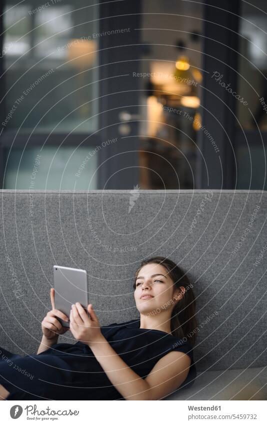 Porträt einer jungen Frau mit digitalem Tablett, die auf einer Couch liegt und in die Ferne schaut Leute Menschen People Person Personen Europäisch Kaukasier