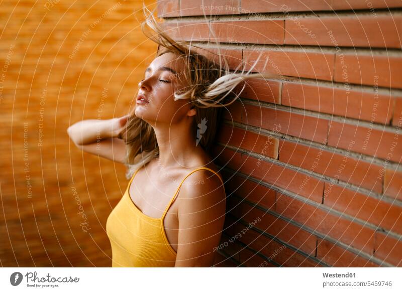 Hübsche junge Frau mit zerzaustem Haar steht gegen eine Ziegelmauer auf dem Balkon Europäer Europäisch Kaukasier kaukasisch eine Person ein Mensch