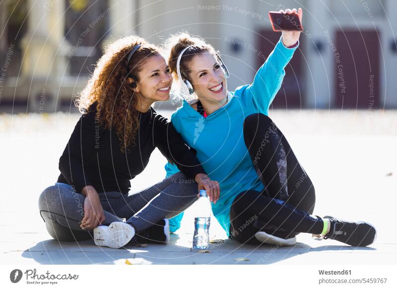 Zwei lächelnde, sportliche junge Frauen, die eine Pause machen und ein Selfie machen Freundinnen Selfies weiblich Freunde Freundschaft Kameradschaft Sport