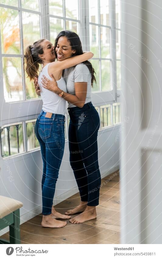 Zwei glückliche Freundinnen umarmen am Fenster zu Hause Zuhause daheim Frau weiblich Frauen Glück glücklich sein glücklichsein Umarmung Umarmungen Arm umlegen