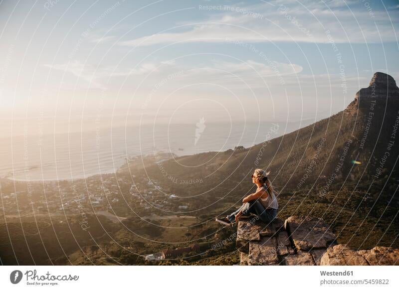 Südafrika, Kapstadt, Kloof Nek, Frau sitzt auf Felsen bei Sonnenuntergang sitzen sitzend weiblich Frauen Sonnenuntergänge Gestein Steine Erwachsener erwachsen