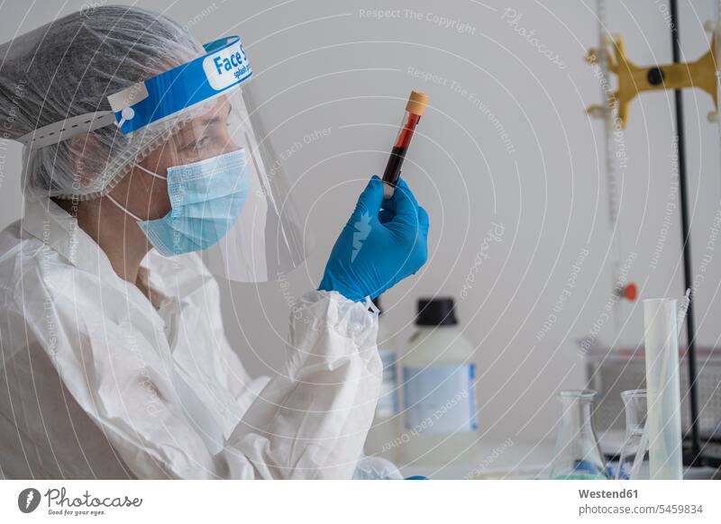 Frau in Schutzkleidung sitzt am Schreibtisch und untersucht Blutprobe Job Berufe Berufstätigkeit Beschäftigung Jobs Tische Arbeitstisch Schreibtische Gesundheit