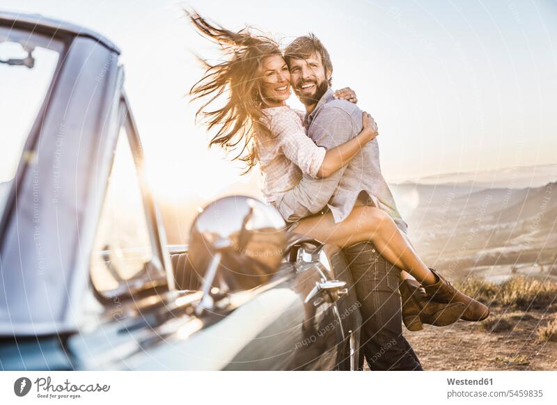 Glückliches Paar beim Cabriolet auf dem Land bei Sonnenuntergang Touristen Hemden KFZ Verkehrsmittel Automobil Autos PKW PKWs Wagen Cabriolets Cabrios Kabrio