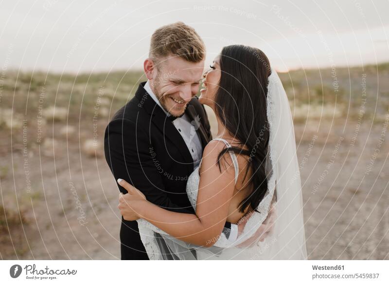 Glücklicher Bräutigam umarmt Braut, während er im Feld gegen den Himmel steht Farbaufnahme Farbe Farbfoto Farbphoto Außenaufnahme außen draußen im Freien