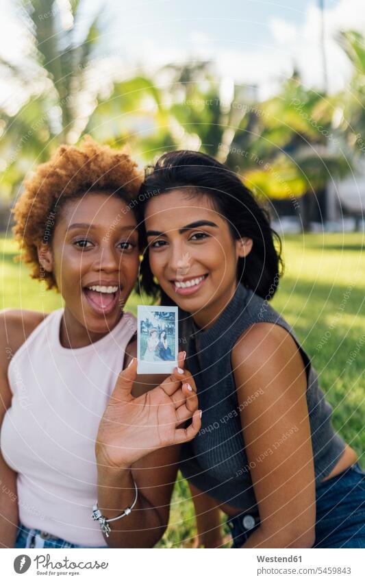 Zwei glückliche Freundinnen zeigen ein Sofortfoto in einem Park Glück glücklich sein glücklichsein Sofortbild Polaroids Sofortbilder vorführen präsentieren