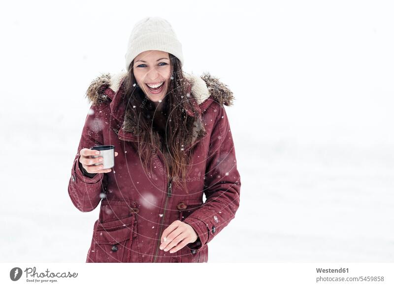 Porträt einer lachenden jungen Frau mit Heissgetränk im Schnee entspannen relaxen Jahreszeiten winterlich Winterzeit begeistert Enthusiasmus enthusiastisch