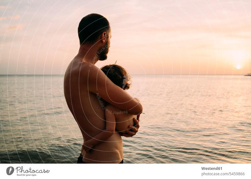 Vater hält kleine Tochter auf dem Arm, während er gemeinsam den Sonnenuntergang am Meer betrachtet Sonnenuntergänge Gemeinsam Zusammen Miteinander betrachten