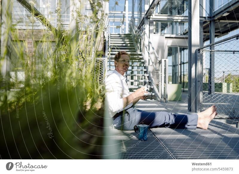 Männliche Fachkraft mit Kaffee entspannt auf dem Boden in der Gärtnerei Farbaufnahme Farbe Farbfoto Farbphoto Deutschland Geschäftsleute Geschäftsperson