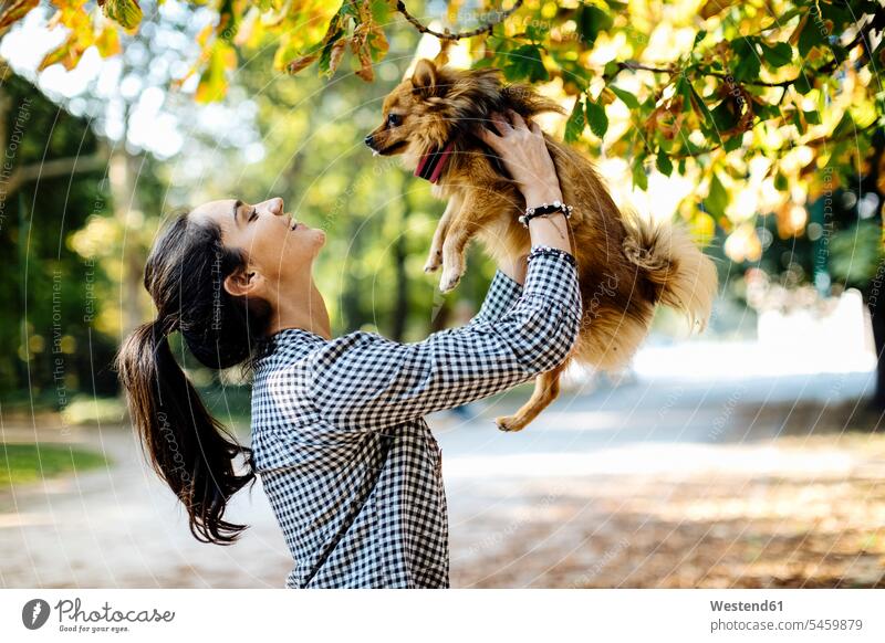 Glückliche junge Frau hält Hund in einem Park Tiere Tierwelt Haustiere Hunde entspannen relaxen freuen Frohsinn Fröhlichkeit Heiterkeit geniessen Genuss