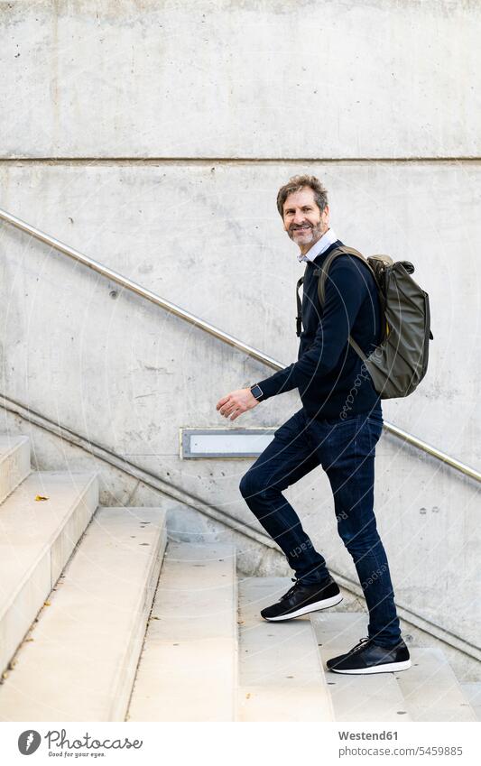 Lächelnde reifen Mann mit einem Rucksack zu Fuß die Treppe hinauf in der Stadt Rucksäcke Männer männlich treppauf staedtisch städtisch lächeln Treppenaufgang