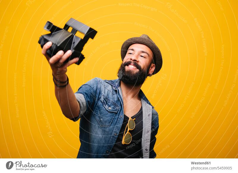 Bärtiger junger Mann im Studio macht Selfie mit Sofortbildkamera Leute Menschen People Person Personen Afrikanisch Afrikanische Abstammung dunkelhäutig Farbige