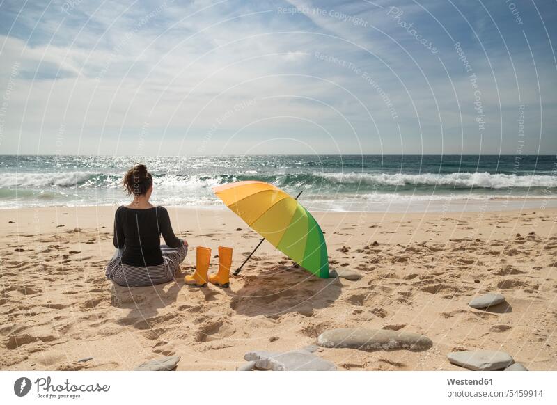 Frau mit buntem Schirm am Strand sitzend, Rückansicht Gummistiefel Sonnenbad sonnenbaden sich sonnen weiblich Frauen Stiefel Schuh Schuhe Erwachsener erwachsen