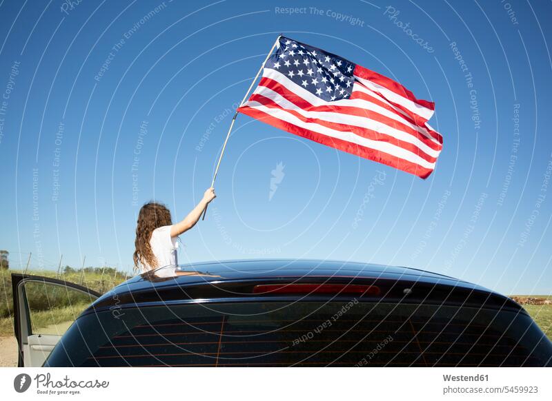 Mädchen hält amerikanische Flagge aus einem Auto unter blauem Himmel halten Fahnen Flaggen blauer blaues Wagen PKWs Automobil Autos weiblich Farbe Farbtöne
