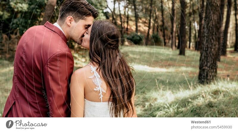 Rückenansicht von Braut und Bräutigam, die sich im Wald küssen Forst Wälder Hochzeit heiraten Heirat Hochzeiten Küsse Kuss Bräute Bräutigame Brautpaar