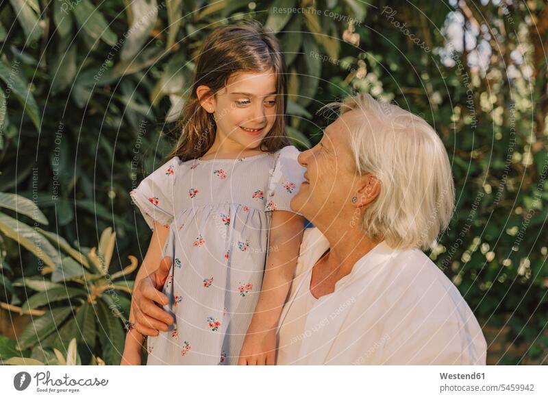 Lächelnde ältere Frau betrachtet niedliche Enkelin vor Pflanzen im Hof Farbaufnahme Farbe Farbfoto Farbphoto Spanien Freizeitbeschäftigung Muße Zeit Zeit haben