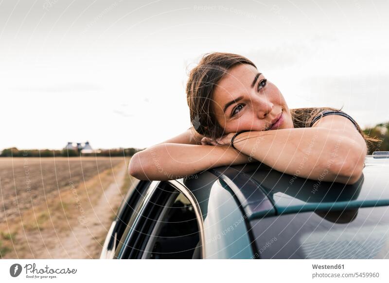 Lächelnde junge Frau schaut aus dem Schiebedach eines Autos Wagen PKWs Automobil Schiebedaecher Schiebedächer weiblich Frauen schauen sehend lächeln
