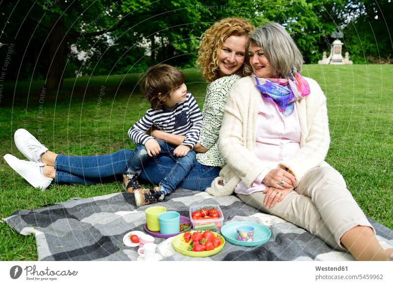 Glücklicher Junge genießt Picknick mit Mutter und Großmutter im öffentlichen Park Farbaufnahme Farbe Farbfoto Farbphoto Außenaufnahme außen draußen im Freien