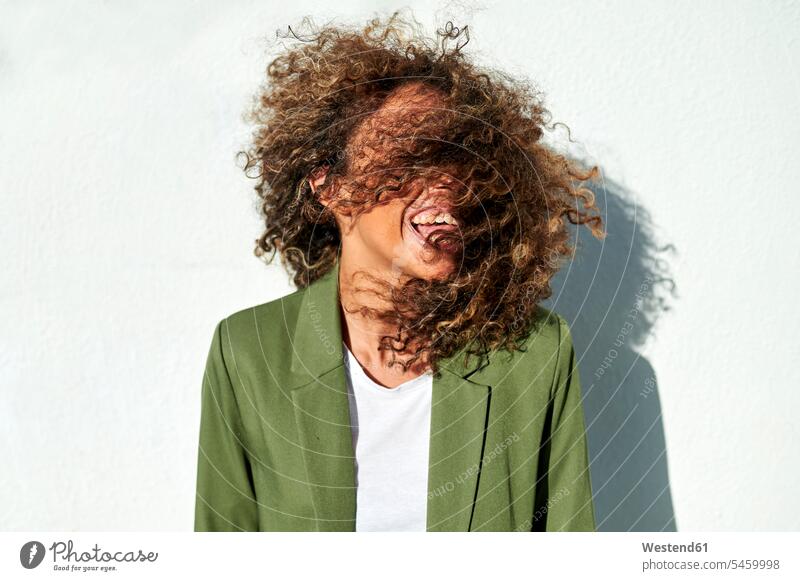 Verspielte Frau wirft bei Sonnenschein lockiges Haar gegen die weiße Wand Farbaufnahme Farbe Farbfoto Farbphoto Außenaufnahme außen draußen im Freien Tag