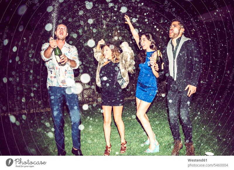Junger Mann öffnet Champagner, während Freunde nachts im Freien auf einer Party tanzen Farbaufnahme Farbe Farbfoto Farbphoto Freizeitbeschäftigung Muße Zeit