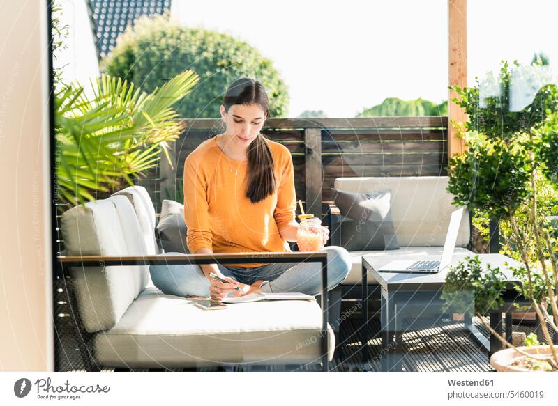 Junge Frau sitzt auf der Couch auf der Terrasse mit gesundem Getränk und Notizbuch Leute Menschen People Person Personen Europäisch Kaukasier kaukasisch 1 Ein
