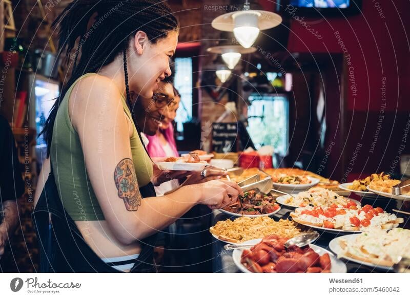 Glückliche Freunde beim Essen vom Buffet in einem Restaurant Leute Menschen People Person Personen Europäisch Kaukasier kaukasisch gemischtrassig