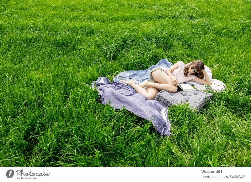 Entspannte Frau liegt auf einer Wiese und liest ein Buch Leute Menschen People Person Personen Europäisch Kaukasier kaukasisch 1 Ein ein Mensch nur eine Person