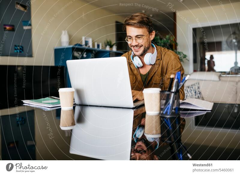 Lächelnder Mann arbeitet zu Hause am Tisch mit einem Laptop Job Berufe Berufstätigkeit Beschäftigung Jobs geschäftlich Geschäftsleben Geschäftswelt