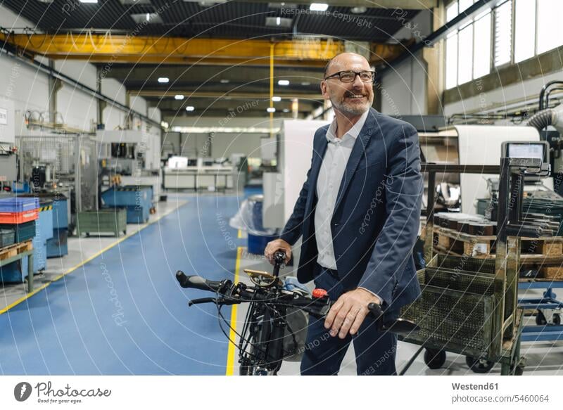 Lächelnder Geschäftsmann mit Fahrrad in einer Fabrik Job Berufe Berufstätigkeit Beschäftigung Jobs geschäftlich Geschäftsleben Geschäftswelt Geschäftsperson