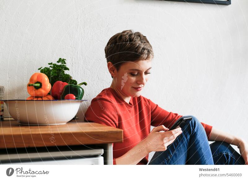 Frau sitzt in der Küche und hört Smartphone-Nachrichten ab Küchen simsen SMS Textnachricht iPhone Smartphones sitzen sitzend lesen Lektüre Soziale Medien
