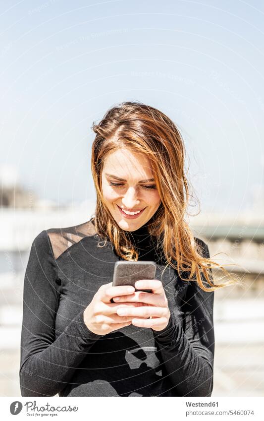 Porträt einer lächelnden Frau, die ein Smartphone im Freien benutzt weiblich Frauen benutzen iPhone Smartphones Portrait Porträts Portraits Erwachsener