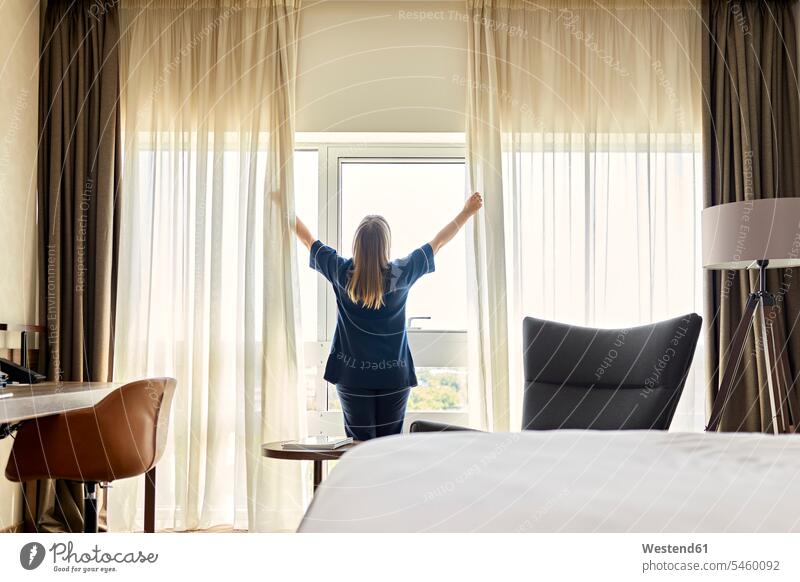 Zimmermädchen öffnet Vorhänge am Fenster im Hotelzimmer Farbaufnahme Farbe Farbfoto Farbphoto Innenaufnahme Innenaufnahmen innen drinnen Millennials