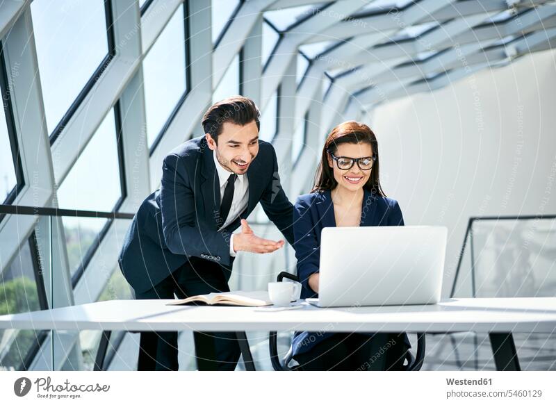 Lächelnde Geschäftsfrau und Geschäftsmann mit Laptop am Schreibtisch im modernen Büro Arbeitstisch Schreibtische Businessmann Businessmänner Geschäftsmänner