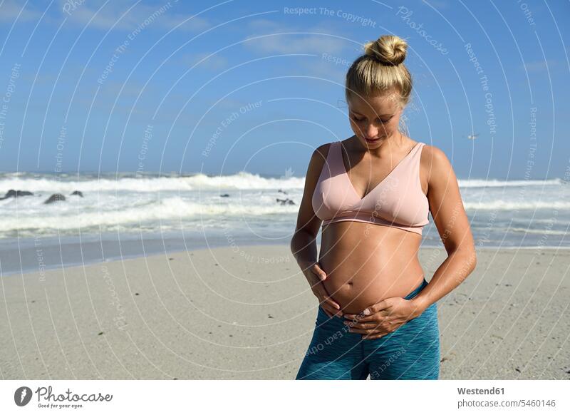 Aktive schwangere Frau am Strand, die ihren Bauch berührt Bäuche Schwangere Portrait Porträts Portraits weiblich Frauen aktiv berühren Berührung anfassen Beach