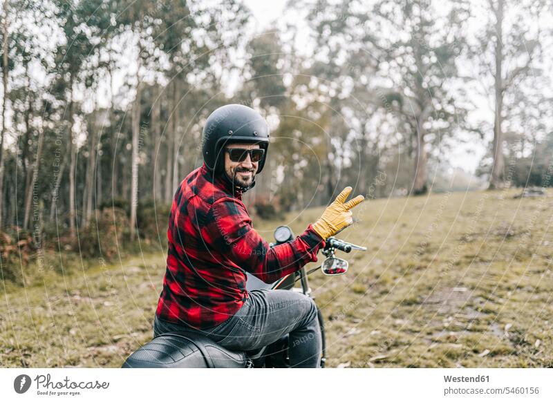 Lächelnder männlicher Motorradfahrer gestikuliert, während er den Wald auf dem Motorrad erkundet Farbaufnahme Farbe Farbfoto Farbphoto Spanien Außenaufnahme