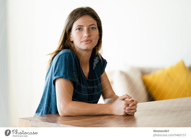 Porträt einer selbstbewussten jungen Frau, die zu Hause am Tisch sitzt Polster T-Shirts Couch Couches Liege Sofas Tische Holztische sitzend entspannen relaxen