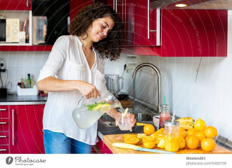 Junge Frau in der Küche zu Hause gießt Limonade in Glas Leute Menschen People Person Personen Europäisch Kaukasier kaukasisch 1 Ein ein Mensch eine