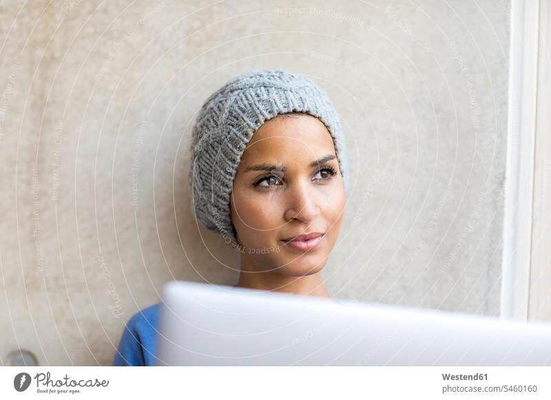 Porträt einer nachdenklichen jungen Frau mit Laptop, die aus dem Fenster schaut Notebook Laptops Notebooks schauen schauend anschauen betrachten weiblich Frauen