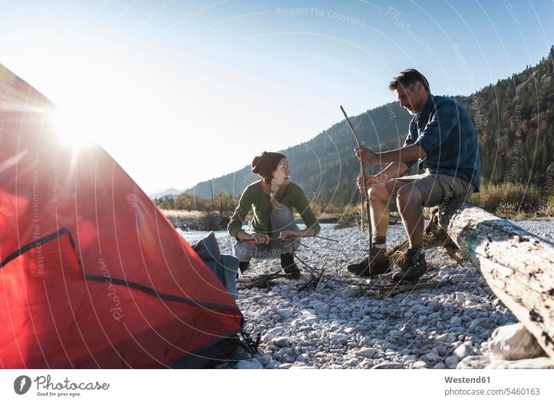 Älteres Paar zeltet am Flussufer, mit Holz für ein Lagerfeuer Abenteuer abenteuerlich zelten Zelt Zelte hoelzern hölzern Camping Campen Naturerlebnis Pärchen