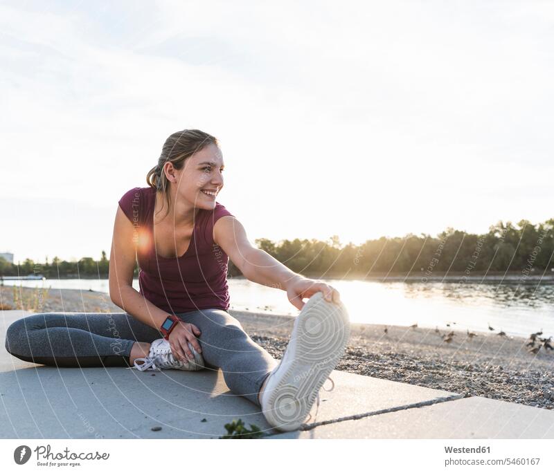 Junge Frau sitzt auf dem Boden am Fluss und wärmt sich für das Training auf Fitness fit Gesundheit gesund dehnen strecken aufwärmen sich aufwärmen